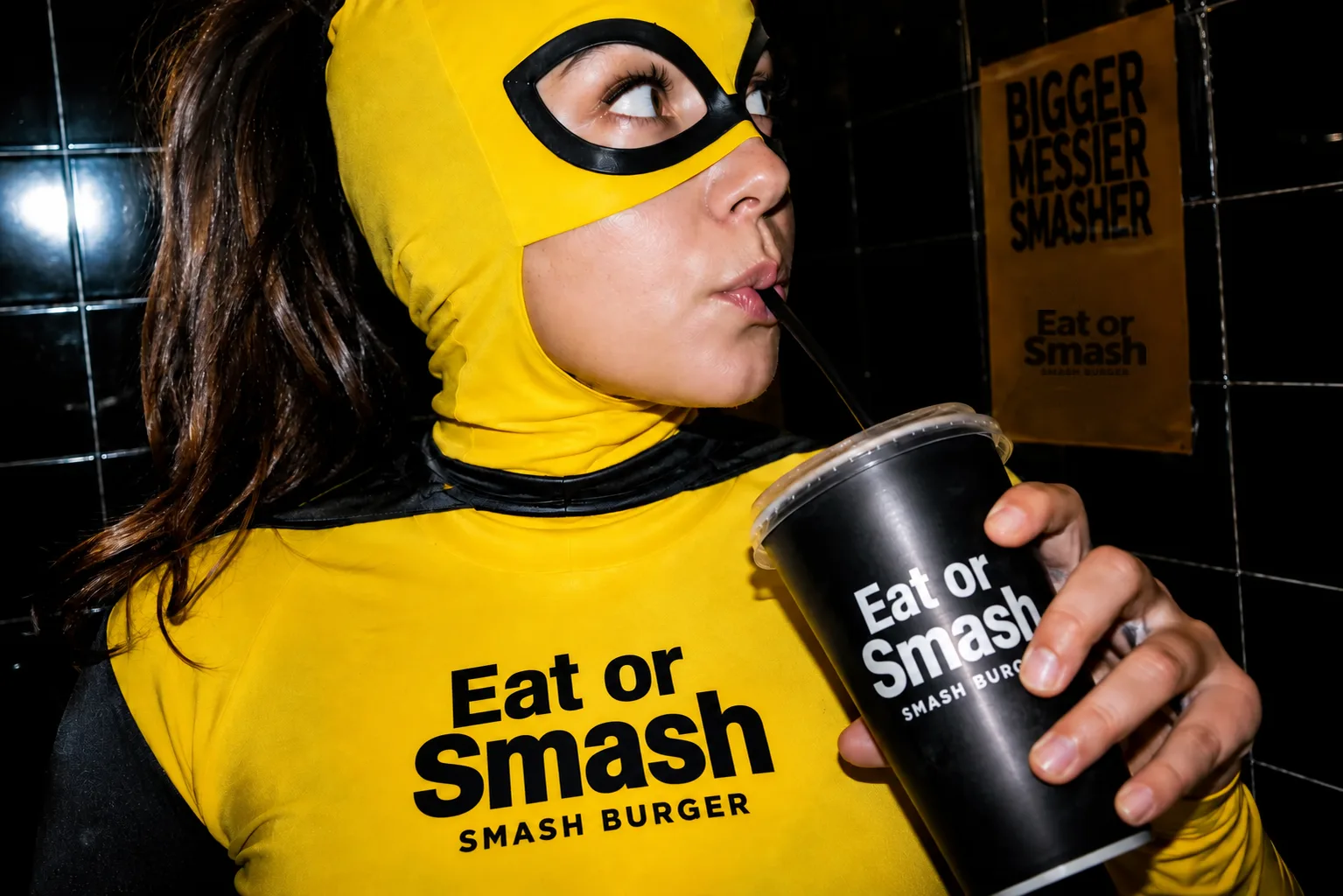 Ragazza con la maschera gialla di How I Met Your Smash che beve dal bicchiere del locale